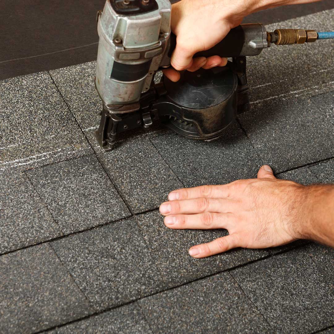 man installing shingles on roof with nail gun