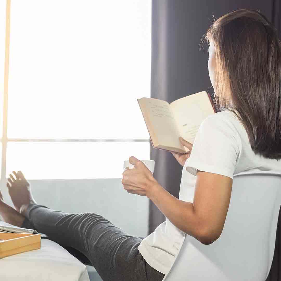 woman lounging near window, reading, drinking coffee