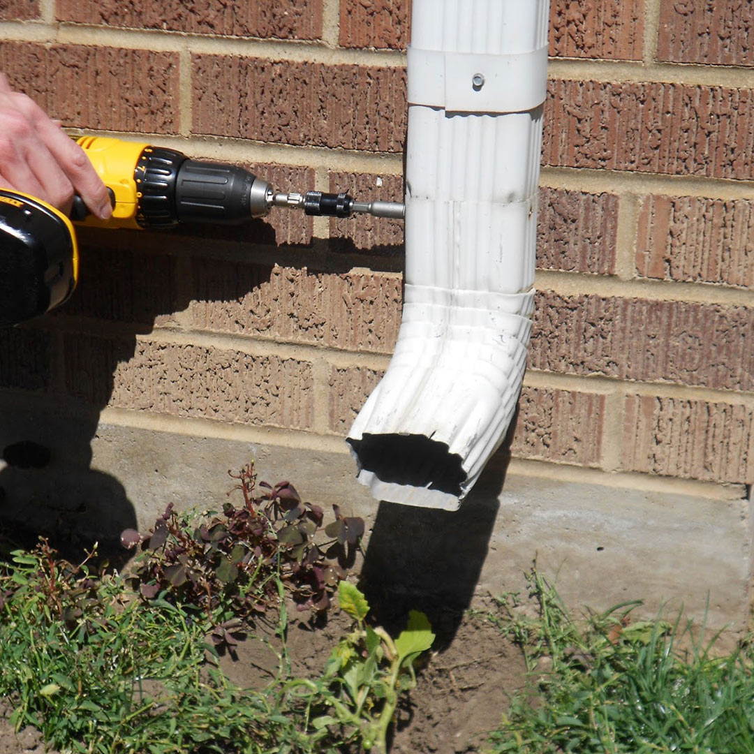 man drilling gutter downspout in place